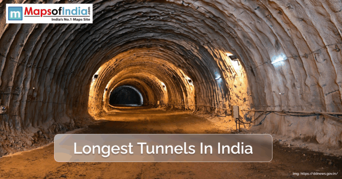 A view inside a large, illuminated tunnel in India, showcasing rough rock walls and ceiling with construction lights, representing one of the country's longest tunnels.