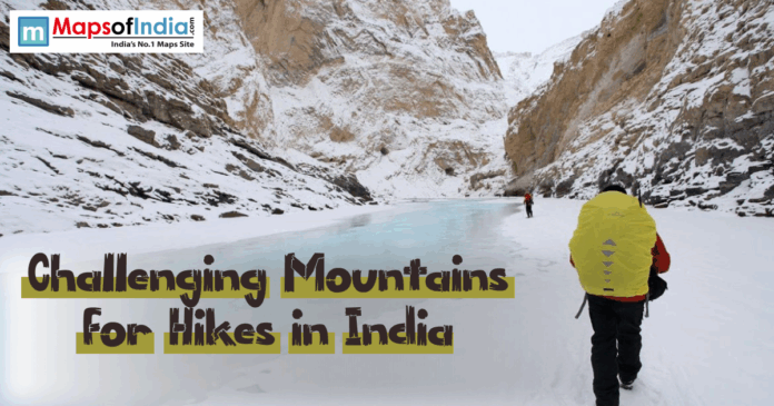 Trekkers hiking on a frozen river surrounded by snow-covered mountains in India – representing challenging mountain hikes