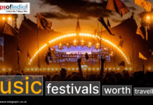 Music Festivals Worth Travel For A large outdoor music festival at sunset with a crowd of people holding flags, facing a brightly lit stage with an illuminated arch and Screens, creating a vibrant concert atmosphere.