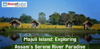 Majuli Island: Exploring Assam’s Serene River Paradise Scenic view of Majuli Island in Assam featuring traditional wooden huts on stilts beside a calm water body, surrounded by lush green fields and trees under a clear blue sky.