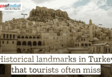 Historical Landmarks in Turkey That Tourists Often Miss An old stone city built into a hillside in Turkey, featuring traditional Artuqid architecture with domed buildings and tall minarets under a cloudy sky. The image includes a "Maps of India" logo and text overlay that reads, "Historical landmarks in Turkey that tourists often miss."