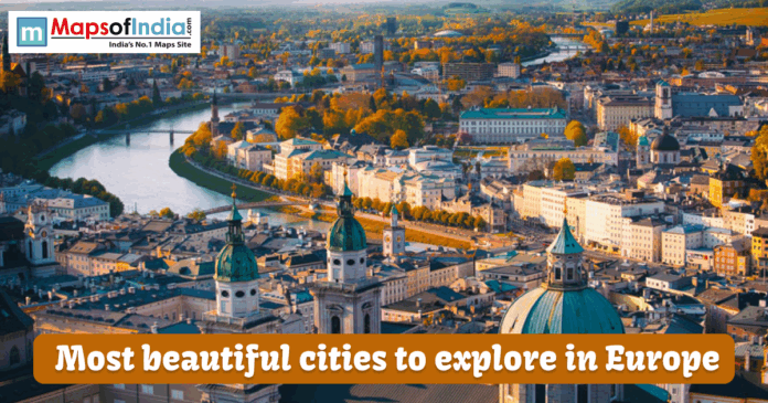 An aerial view of the historic city of Salzburg, Austria, featuring the Salzach River winding through colorful buildings and prominent domed cathedrals under a warm sunset glow. A text overlay at the bottom reads, "Most beautiful cities to explore in Europe."
