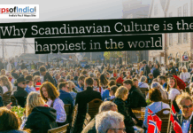 Why Scandinavian Culture Is the Happiest in the World Crowded outdoor café in a Scandinavian waterfront town, with people dining and socializing under sunny skies, Norwegian flags on tables, and historic wooden buildings in the background.