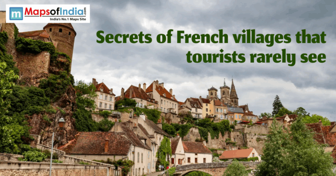Hillside view of a hidden French village with stone tower, colorful houses, church spires, and a bridge under a cloudy sky.