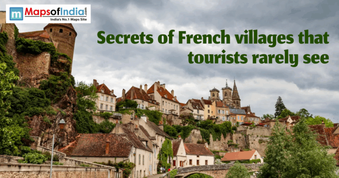 Hillside view of a hidden French village with stone tower, colorful houses, church spires, and a bridge under a cloudy sky.