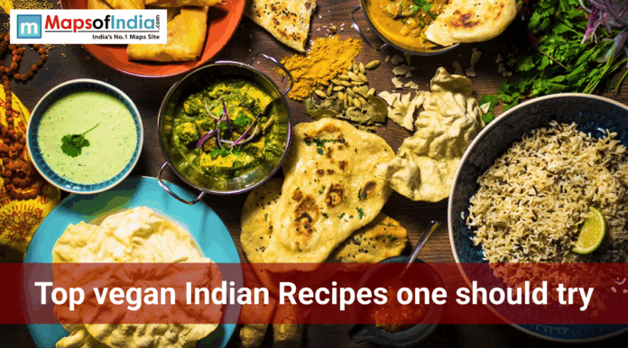 Overhead view of a vegan Indian meal spread with rice, naan, curry, chutney, papad, spices, and herbs, featuring the text “Top vegan Indian recipes one should try.”