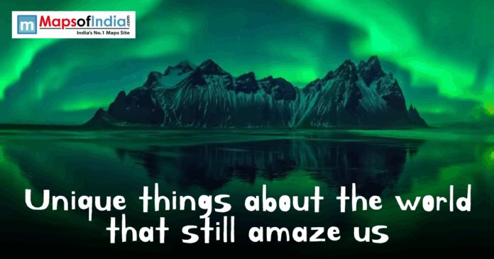 Aurora Borealis glowing bright green behind jagged mountains with the text "Unique things about the world that still amaze us."