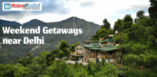Weekend Getaways Near Delhi Scenic mountain landscape with a stone cottage, green hills, and 'Weekend Getaways near Delhi' text. Maps of India logo visible.