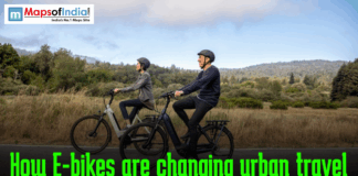 How E-bikes are changing urban travel Two adults wearing helmets ride electric bikes along a scenic road with green hills in the background, with the text “How E-bikes are changing urban travel” and a Maps of India logo displayed