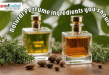 Natural Perfume Ingredients You Should Know Two glass bottles of amber and yellow perfume oil sit on a wooden surface, surrounded by fresh sprigs of rosemary, green leaves, and small seeds.