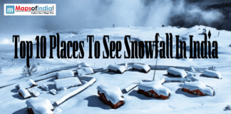 Top 10 Places To See Snowfall in India A snowy mountain landscape in India featuring small wooden huts covered in thick snow with text overlay reading "Top 10 Places To See Snowfall In India" and a Maps of India logo.