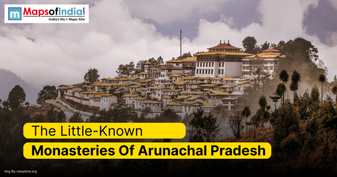 A panoramic view of a large monastery complex nestled amidst lush green hills and misty clouds in Arunachal Pradesh, India, showcasing traditional Tibetan-style architecture with white walls and golden-yellow rooftops.